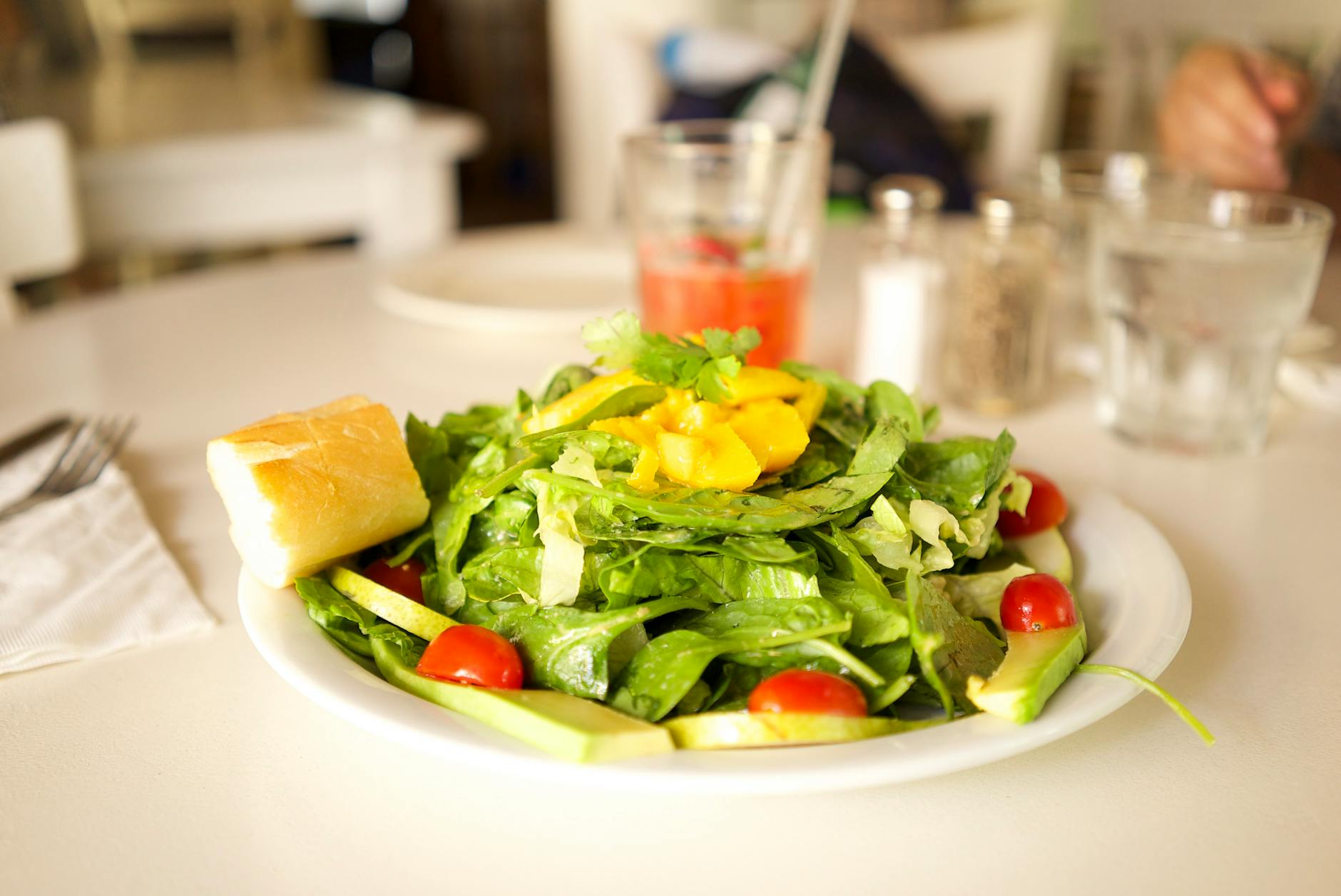 Healthy green salad with cherry tomatoes, lettuce, and mango on a white plate with bread.