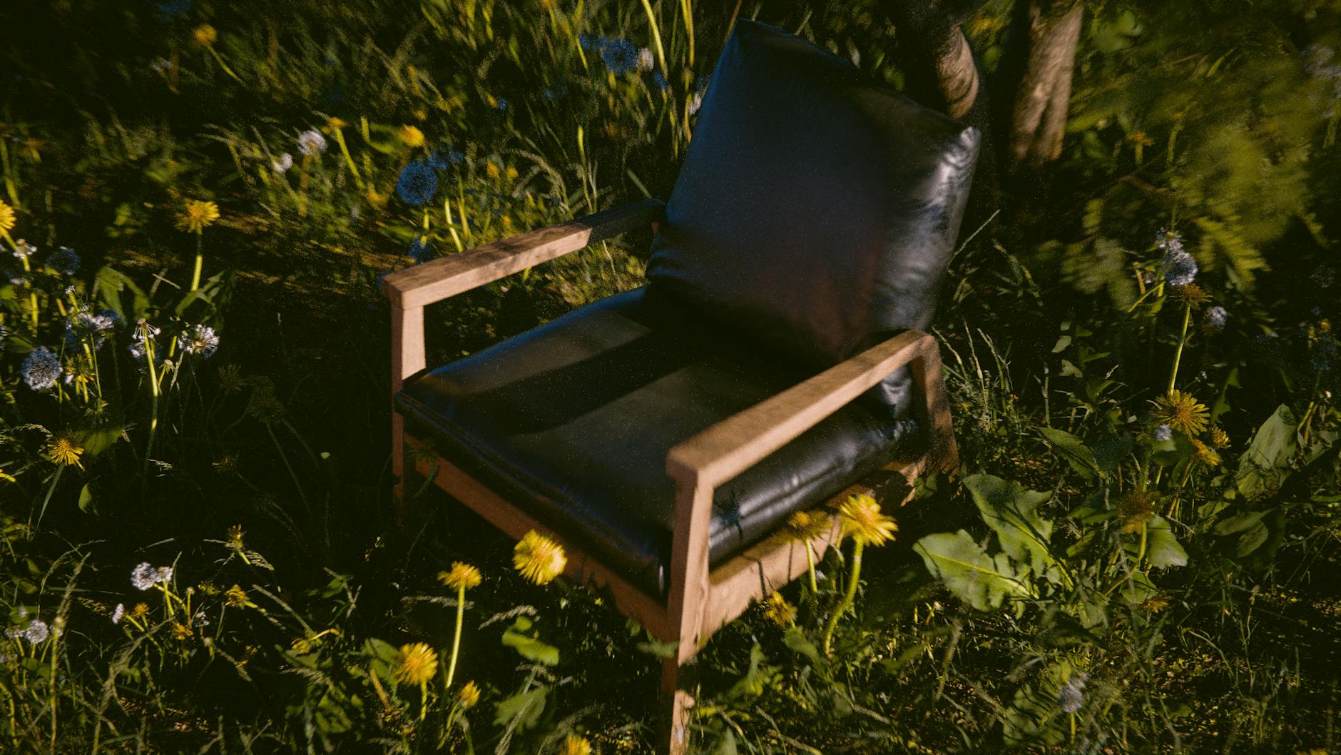 Cozy black chair on wooden frame amidst blooming meadow flowers, offering a serene outdoor retreat.