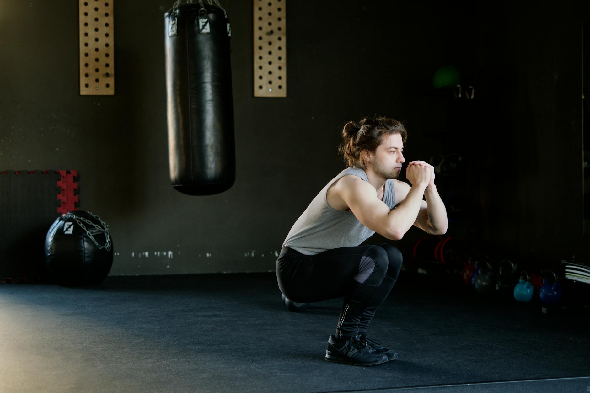 A man is doing squats in a gym with a punching bag. The setting appears stylish and focused on fitness.