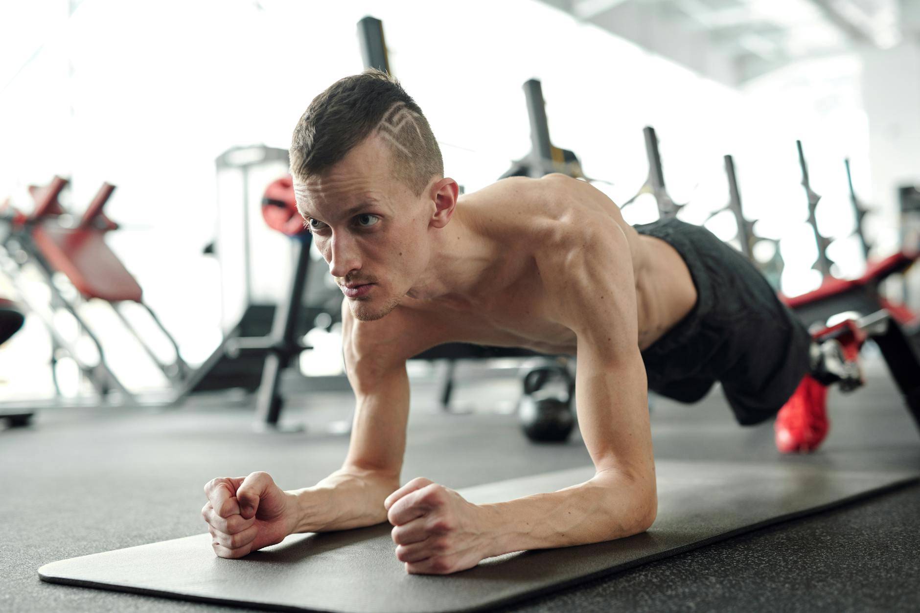 A shirtless man with a prosthetic leg planks on a yoga mat in a gym, showcasing fitness and determination.